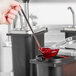A person pouring red liquid into a black container using a Master Bilt pump and jar assembly.