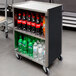 A Lakeside metal utility cart with shelves of soda and soft drinks on wheels.