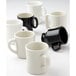 A group of six white Tuxton coffee mugs with black handles and rims.