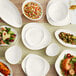 A table with Acopa Nova cream white triangle stoneware plates and bowls of food on it.