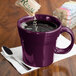 A purple Fiesta tapered mug on a counter with liquid being poured into it with a spoon.