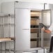 A man in a white apron opening a Beverage-Air reach-in freezer with solid doors.