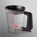 A clear plastic measuring cup with red and black handles.
