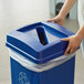 A person holding a Carlisle blue square recycling bin lid with a paper slot.