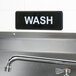 A black and white metal sign that says "Wash" on a wall.