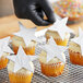 A hand in a black glove holding a star-shaped cupcake with silver shimmer frosting.