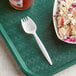 A white plastic spork on a tray with coleslaw.