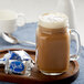 A glass mug of YORK Peppermint Cappuccino with foam and a wrapped candy on a wooden tray.