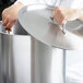 A person in a white coat using a Vollrath stainless steel stock pot lid to cover a large silver stock pot.