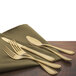 A close-up of a Walco gold stainless steel bouillon spoon and fork on a napkin.
