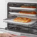 A hand pulls a tray of pizza out of an Avantco Countertop Convection Oven.