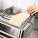 A person using an Imperia stainless steel pasta machine to roll out dough for pasta.