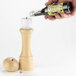 A hand using a wood funnel to refill a pepper mill with black peppercorns.
