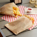 Two Carnival King extra large brown Kraft paper bags with sandwiches and french fries on a table.