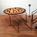 A pizza on a table with a red metal pizza stand with red legs.