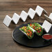 A white American Metalcraft taco holder with 4 or 5 compartments holding 4 tacos on a table.