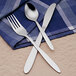 A Libbey stainless steel medium weight tablespoon placed on a blue and white napkin with a knife.