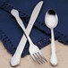 A Libbey stainless steel bouillon spoon and fork on a blue cloth napkin.
