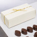 A white candy box with a gold ribbon next to chocolate candies.