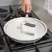 A person using a Vollrath Wear-Ever aluminum non-stick fry pan with a black silicone handle on a stove.
