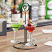 An Acopa metal stand with three martini glasses filled with different colored drinks.