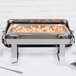A Vollrath Avenger roll top chafer filled with shrimp on a table outdoors.