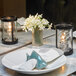 A table set with a Sterno clear finish votive candle and white flowers.