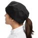 A woman wearing a Mercer Culinary black chef's skull cap.