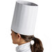 A woman wearing a white Mercer Culinary chef hat.