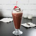 A glass of Ghirardelli Sweet Ground Dark Chocolate cocoa with whipped cream and a cherry.