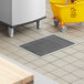 A Regency stainless steel floor trough with a metal grate draining into a yellow bucket on a tile floor.