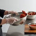 A person in gloves holding two stainless steel mixing bowls of food.