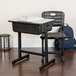 A black Flash Furniture student desk and chair with a notebook on top.