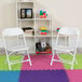 A white Flash Furniture kids plastic folding chair on a colorful mat.