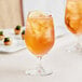 Two Acopa Covella wine glasses filled with orange drinks and lemon slices on a table.
