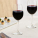A pair of Acopa Covella wine glasses on a table with a glass of wine.