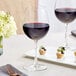 Two Acopa Bordeaux wine glasses filled with red wine on a table with food.