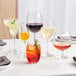 A table with several Acopa Covella burgundy wine glasses filled with different colored drinks.