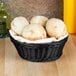 A Tablecraft black round rattan basket filled with bread rolls on a table.
