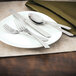 A white plate with silverware on it, including a Walco Classic Scroll stainless steel teaspoon.