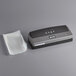 A black and grey rectangular Weston Harvest Guard vacuum sealer on a gray surface with a white sheet underneath.