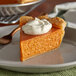 A slice of pumpkin pie with whipped cream on top on a plate.