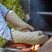 A person cooking burgers on a grill wearing SafeMitt oven mitts.