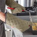 A person wearing SafeMitt flame retardant oven mitts holding a frying pan.