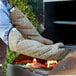 A man wearing SafeMitt flame retardant oven mitts and gloves cooks burgers on a grill.