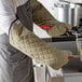 A person wearing SafeMitt flame retardant oven mitts holding a pot with tongs.