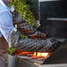 A man in a chef's outfit using a SafeMitt oven mitt to cook meat on a grill.