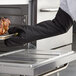 A person in a SafeMitt black oven mitt holding a tray of cooked meat.