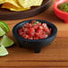 A black Choice thermal plastic molcajete bowl filled with salsa on a wood surface.