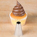 A cupcake with brown frosting piped on top using an Ateco plain metal piping tip.